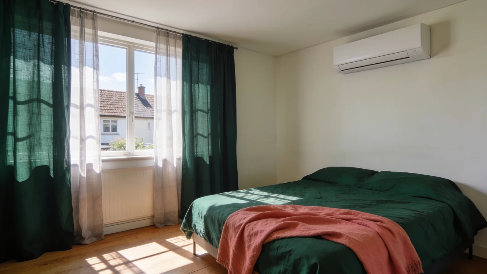 Chambre ensoleillée en été avec une unité murale de pompe à chaleur air/air en hauteur, un radiateur blanc sous la fenêtre et un lit au linge vert